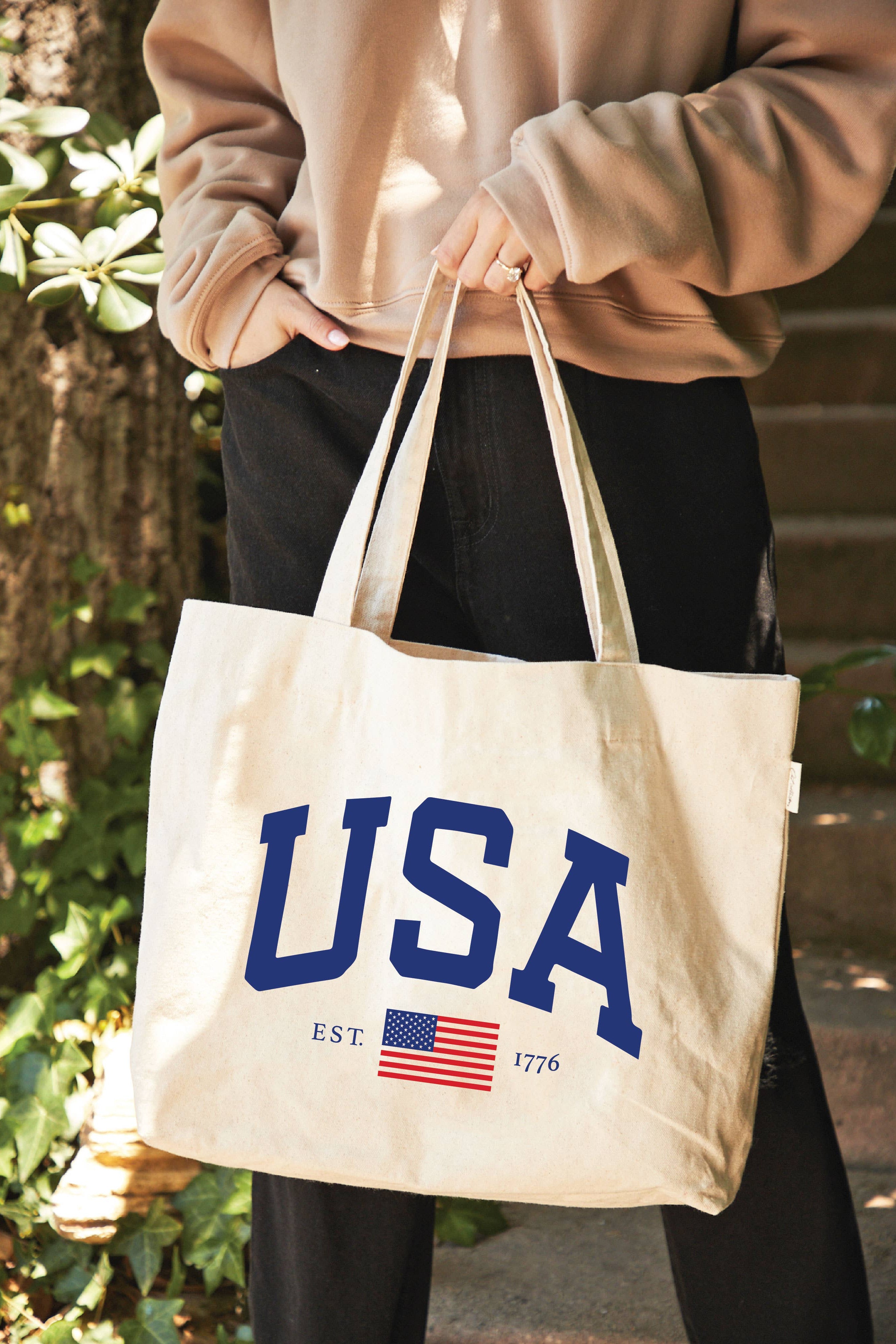 Person holding a tote bag with 'USA' and an American flag design.