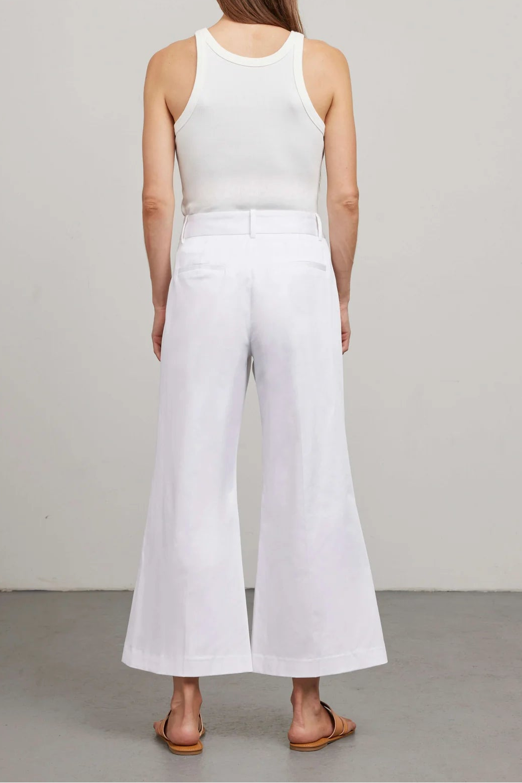 Person wearing a white sleeveless top and wide-leg pants on a plain background