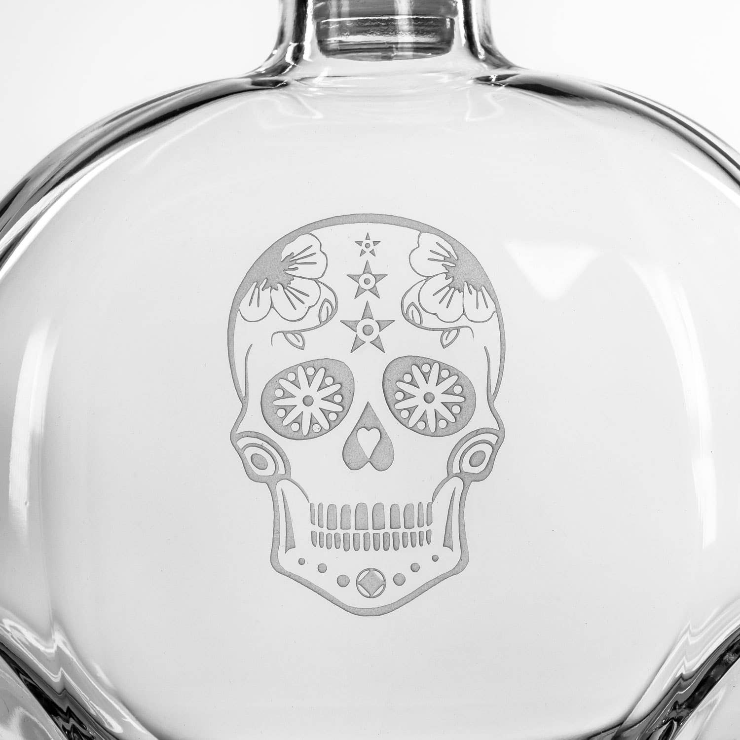 Clear glass bottle with a floral skull design on a white background