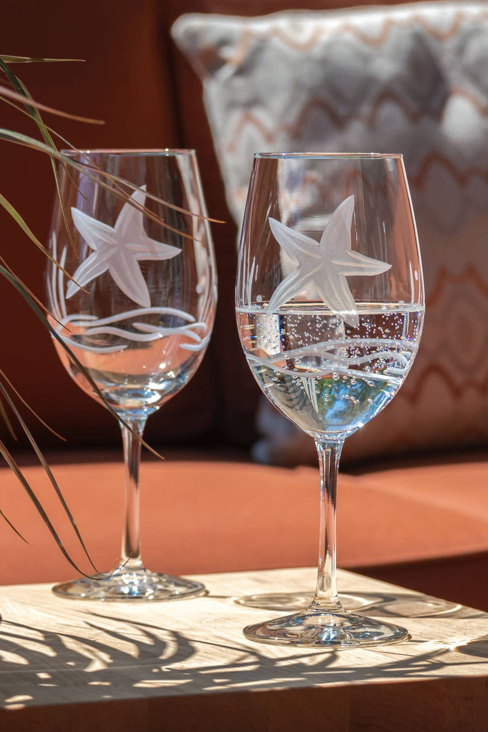 Two wine glasses with starfish designs on a wooden surface outdoors.