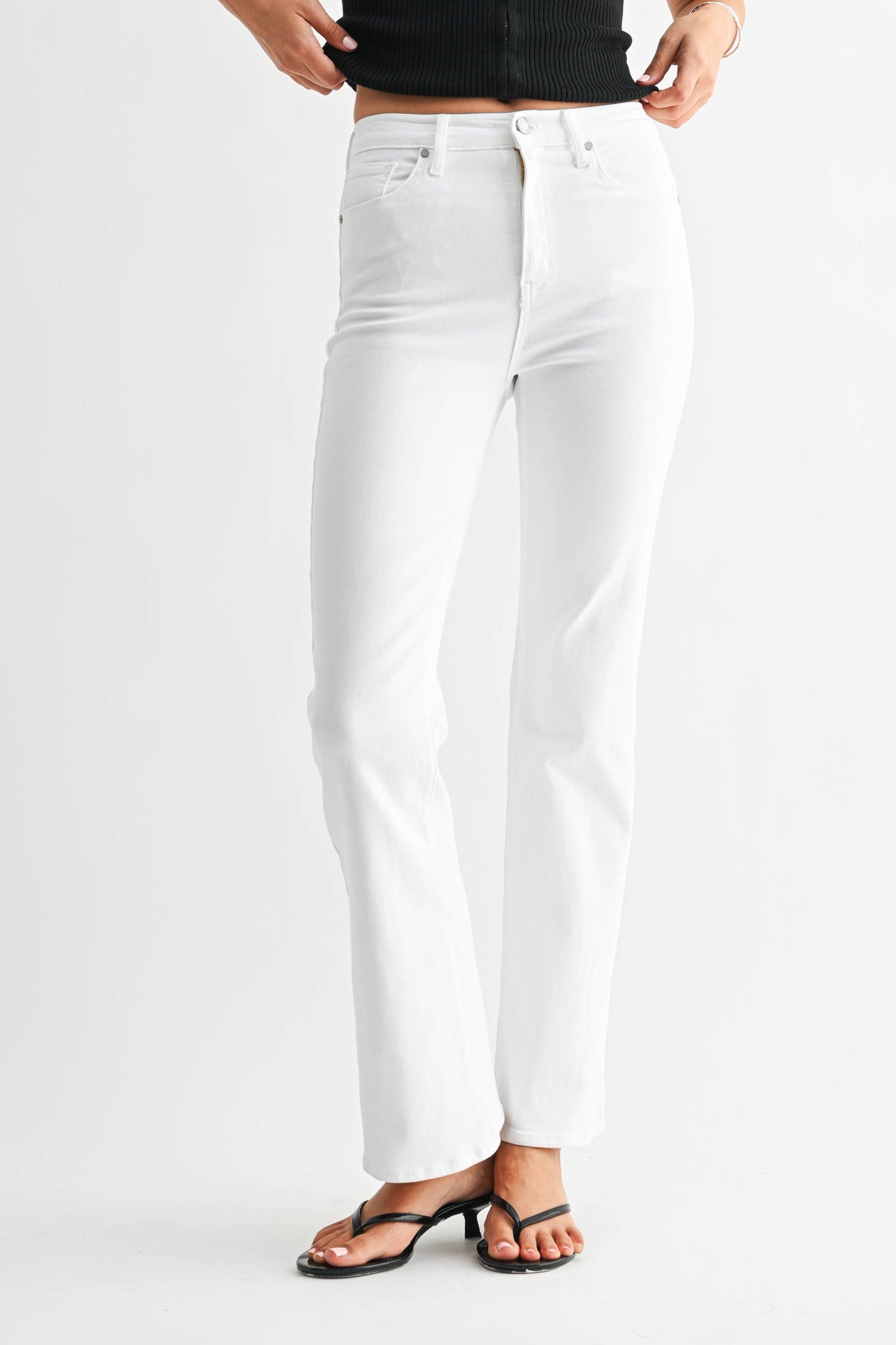 Woman wearing a black tank top and white jeans on a plain background