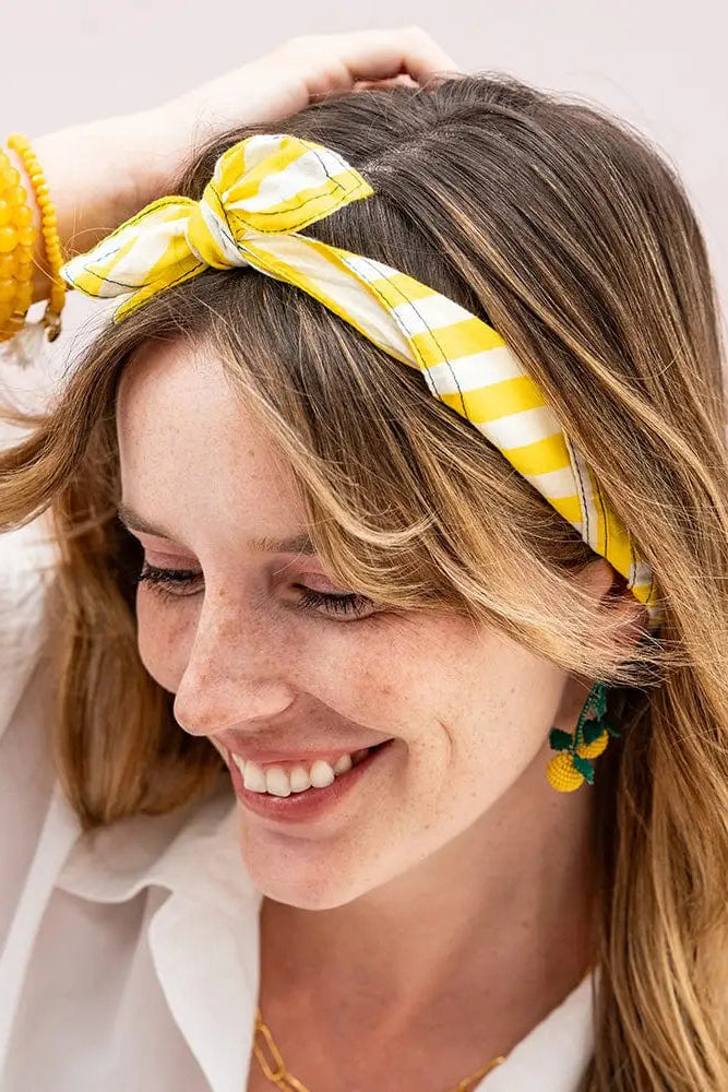 Woman wearing a yellow and white striped headband with a smile on a light background