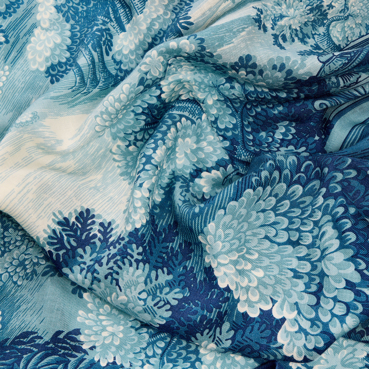 A close-up of draped fabric with a blue and white toile-style floral and landscape print, showing the material's texture and pattern details.