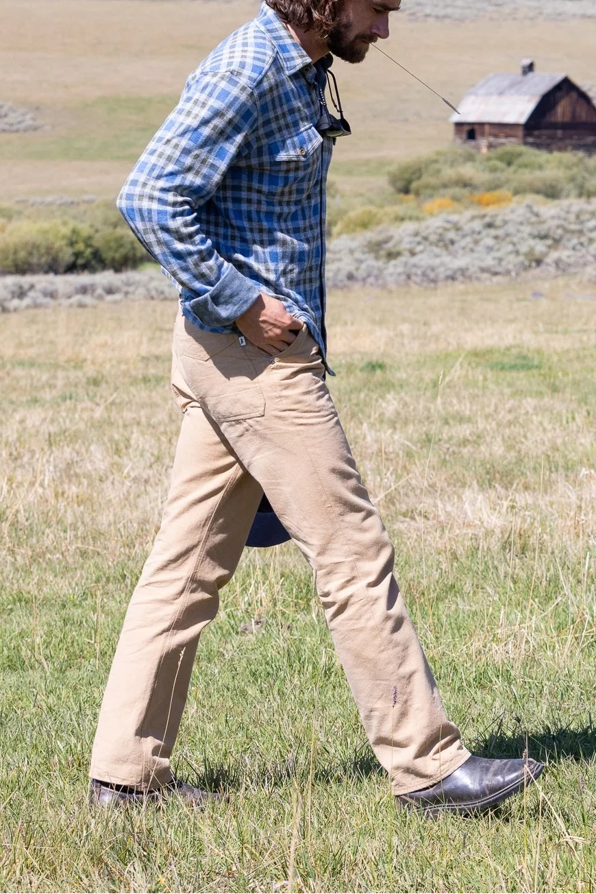 Man walking in a field with a cabin and trees in the background