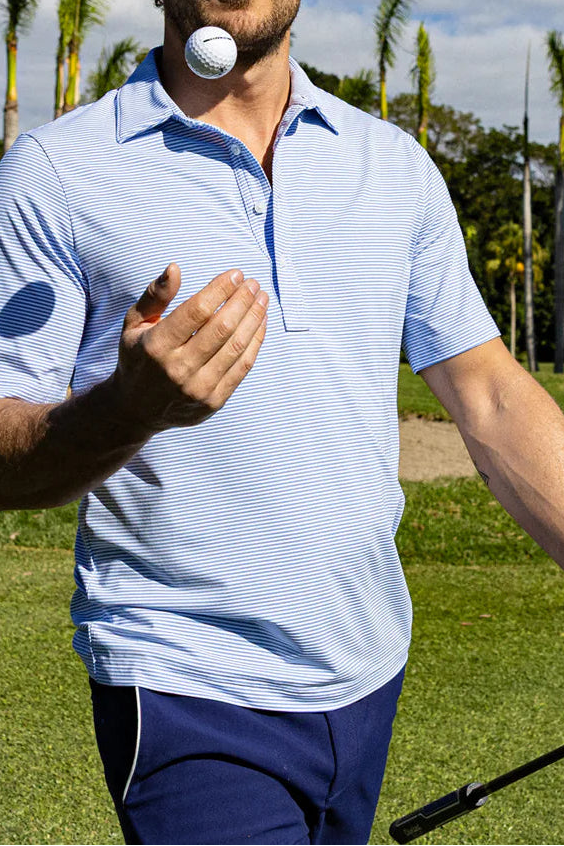 Man on a golf course holding a golf club and ball, with palm trees in the background.