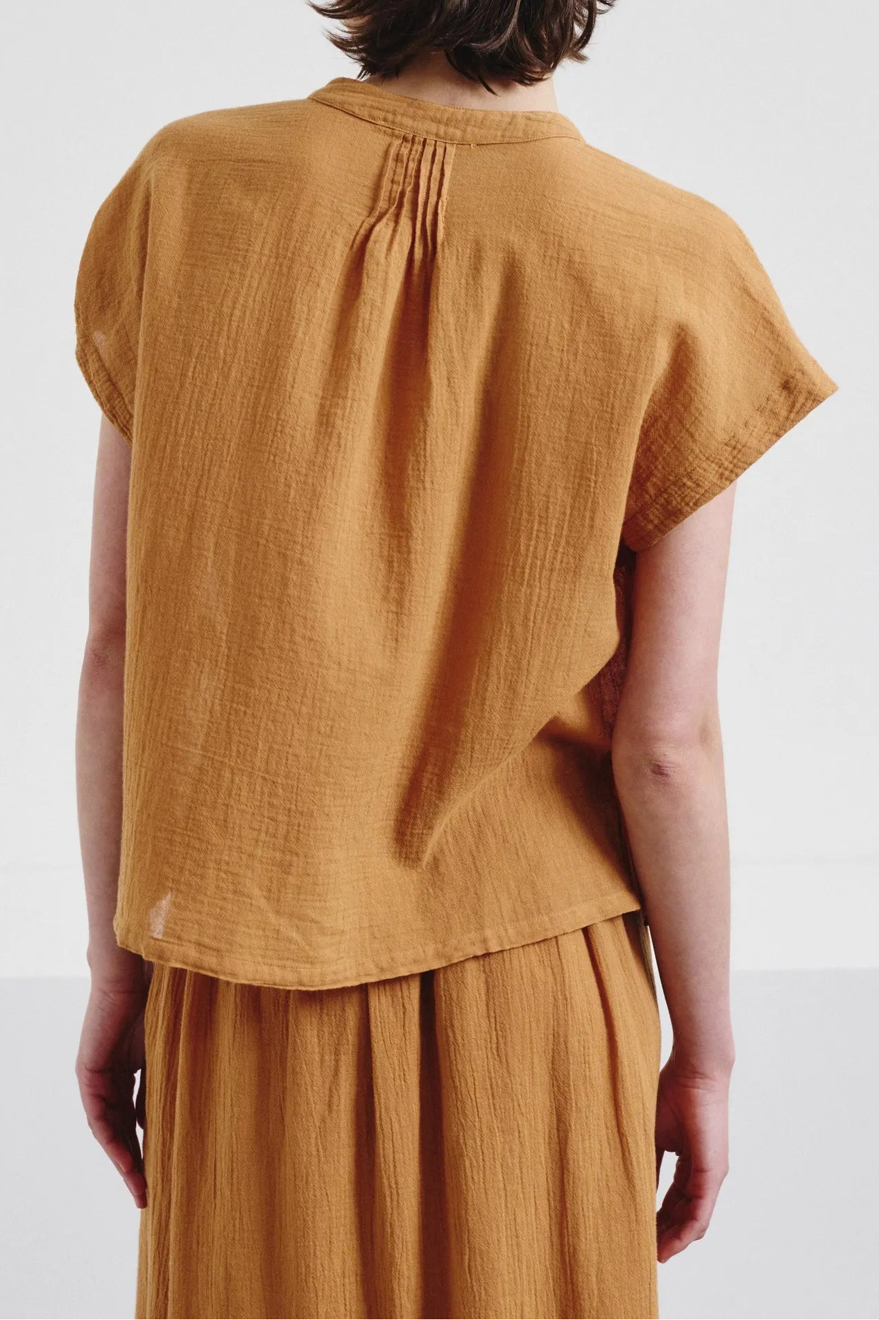 Person wearing a mustard yellow top and skirt set on a white background
