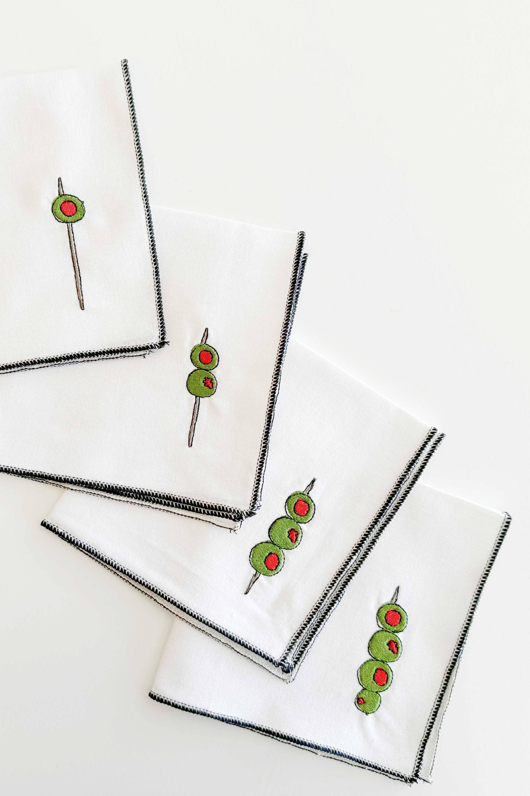 Set of white napkins with black borders and embroidered designs on a white background