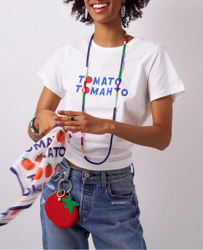 Person wearing a white t-shirt with colorful text, holding a red tomato keychain against a plain background