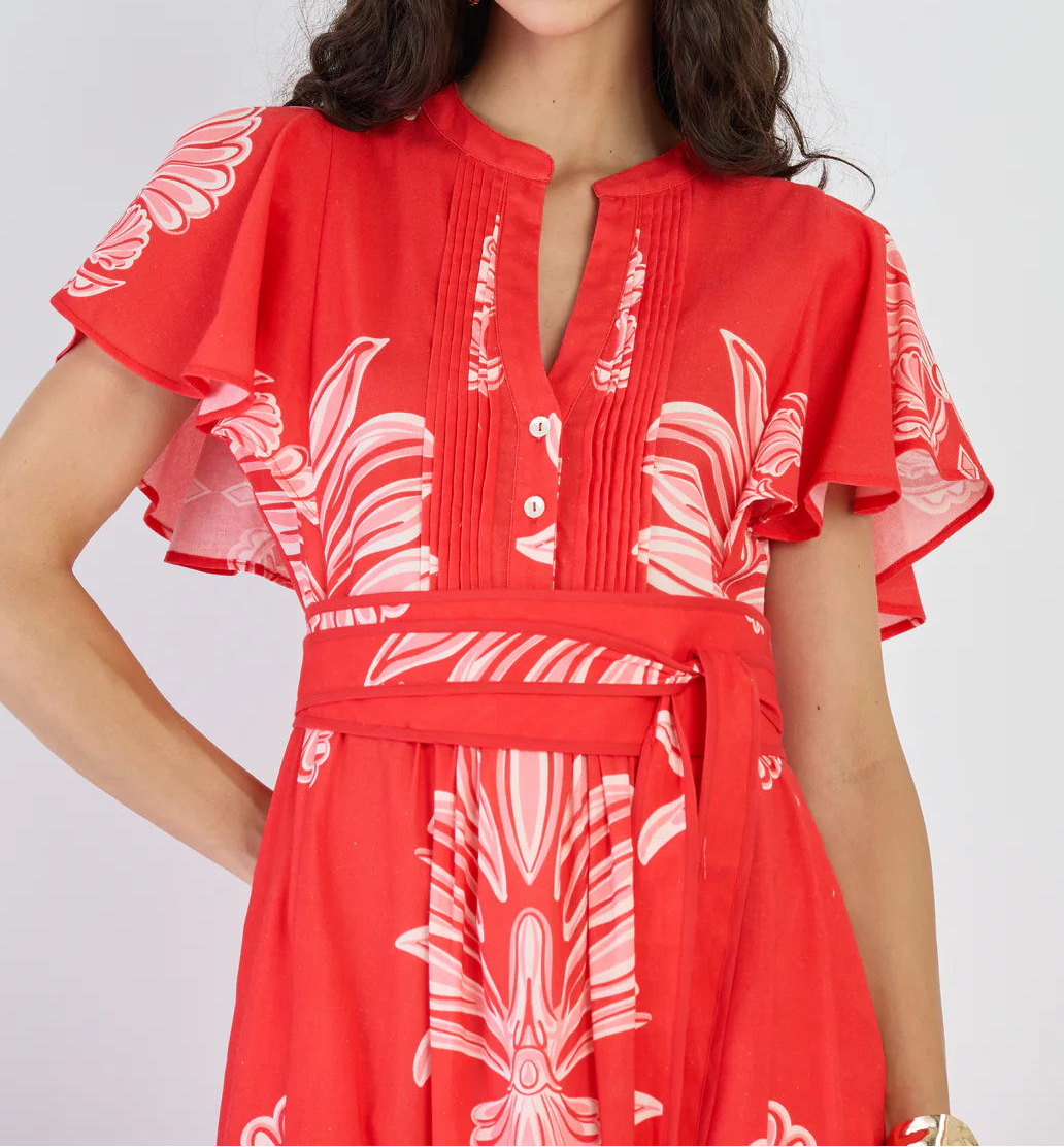 Woman wearing a red dress with white floral patterns on a plain background