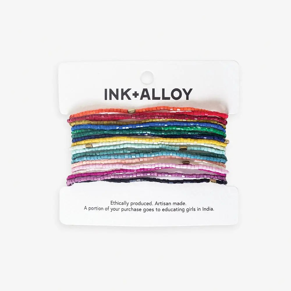 Set of colorful beaded bracelets on a 'INK+ALLOY' branded card with ethical message.