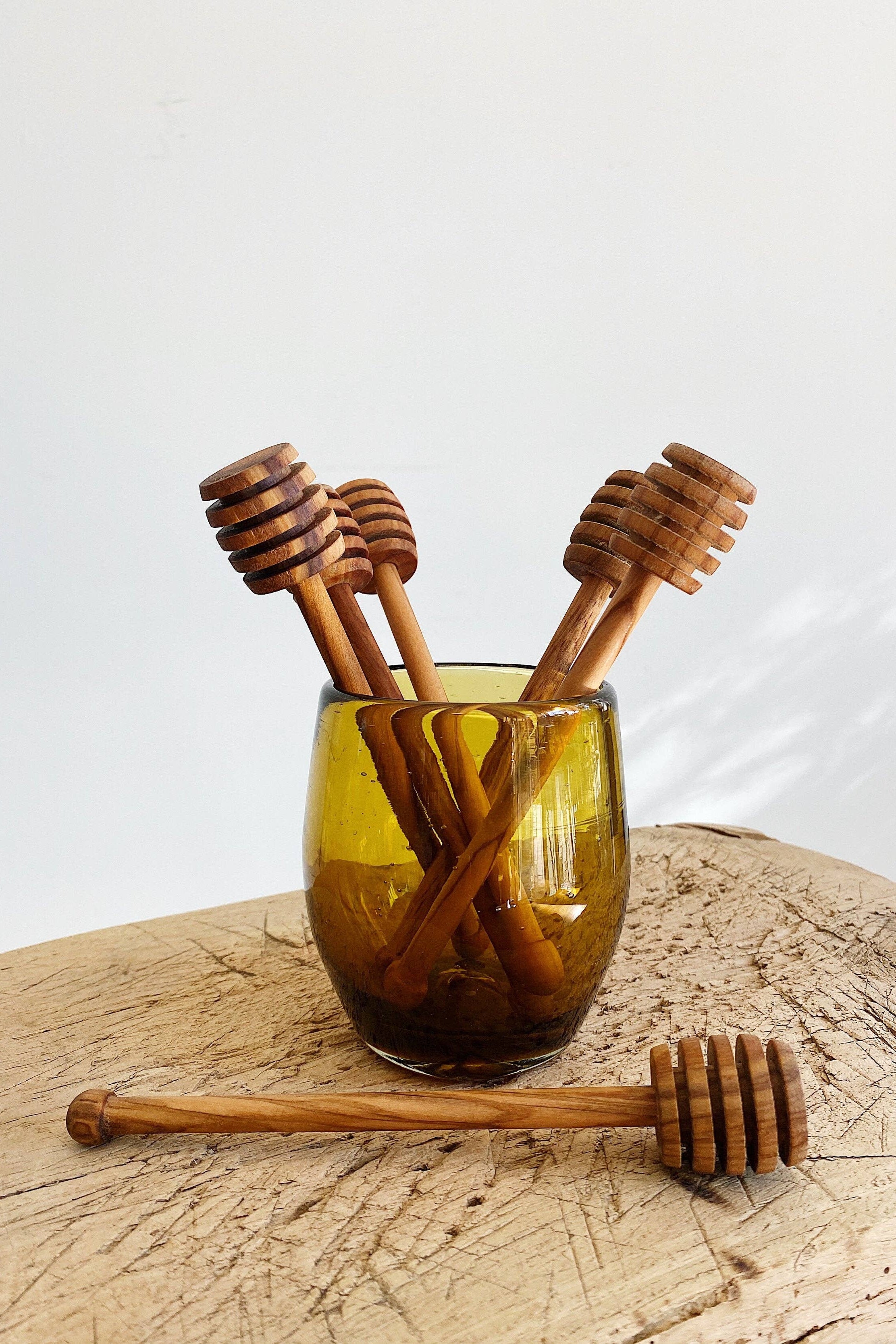 Wooden honey dipper sticks in a glass on a wooden surface with a white background
