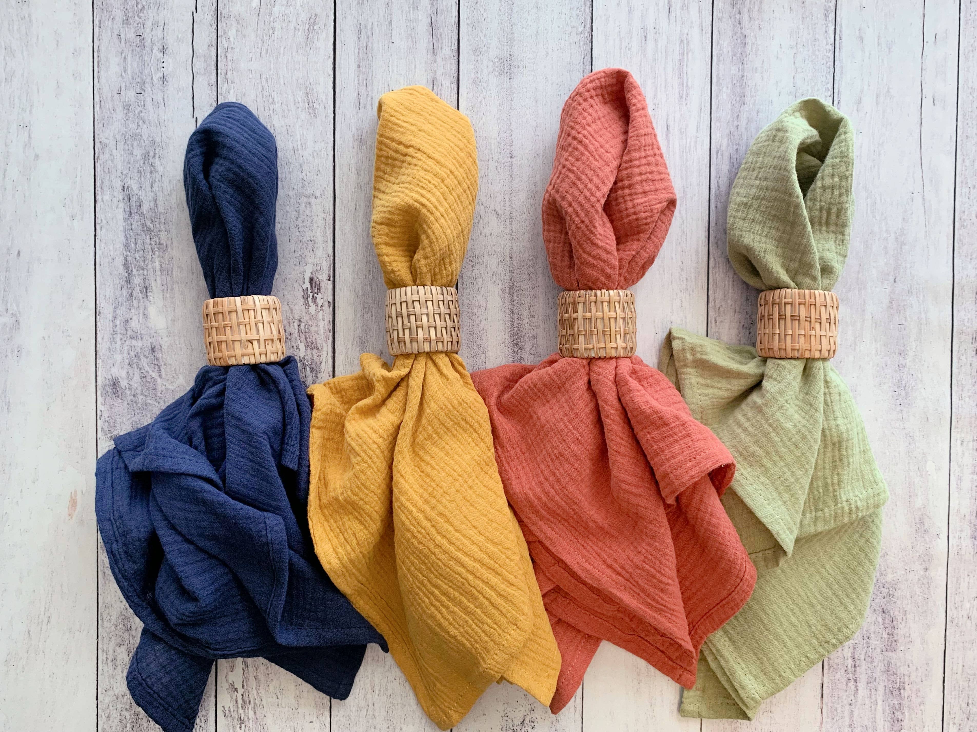 Four colorful napkins with woven bands on a wooden surface