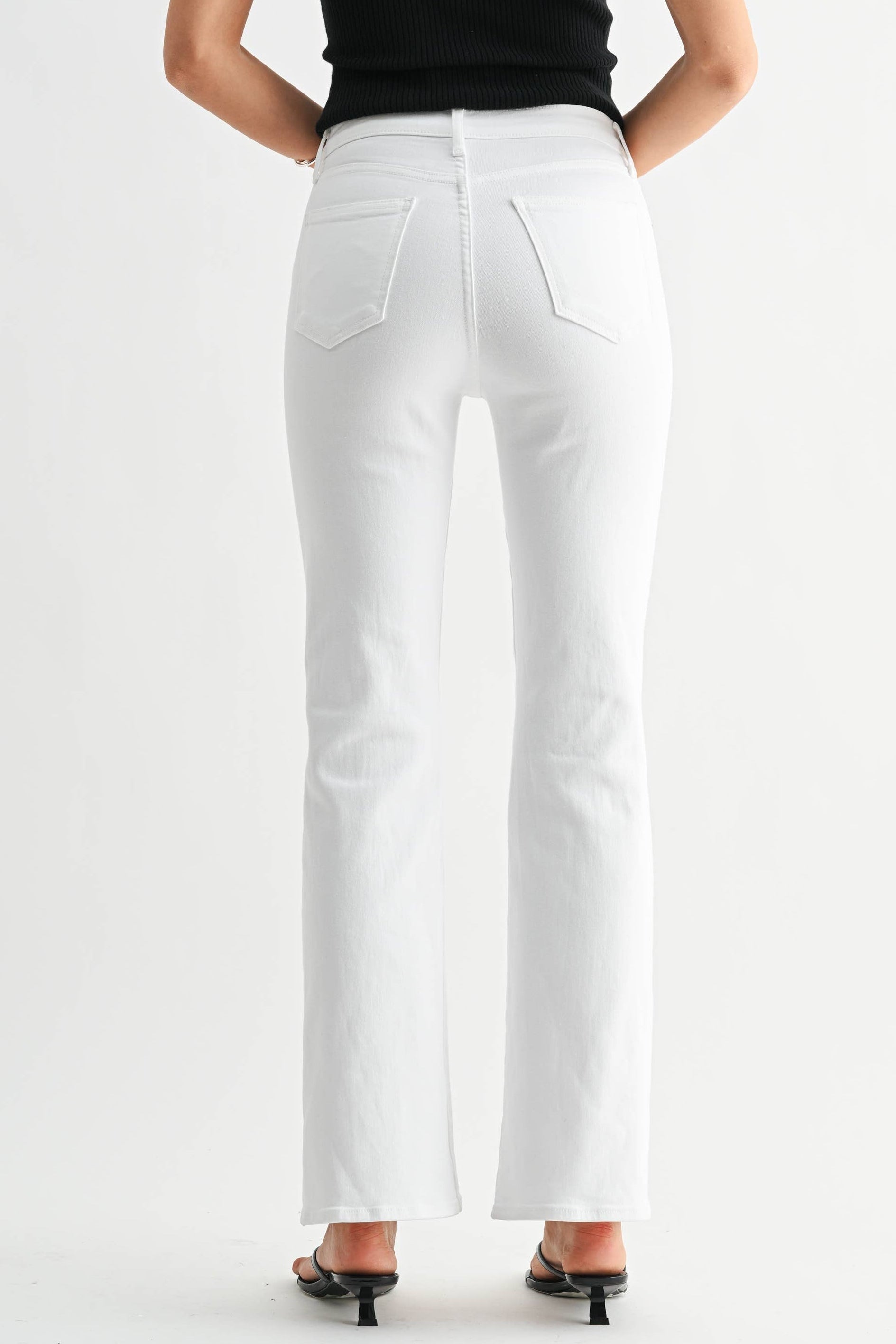 Woman wearing a black tank top and white pants on a white background