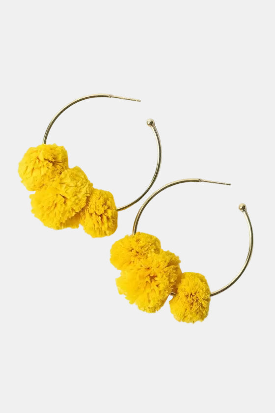 Yellow pom-pom earrings on gold hoop earrings against a white background