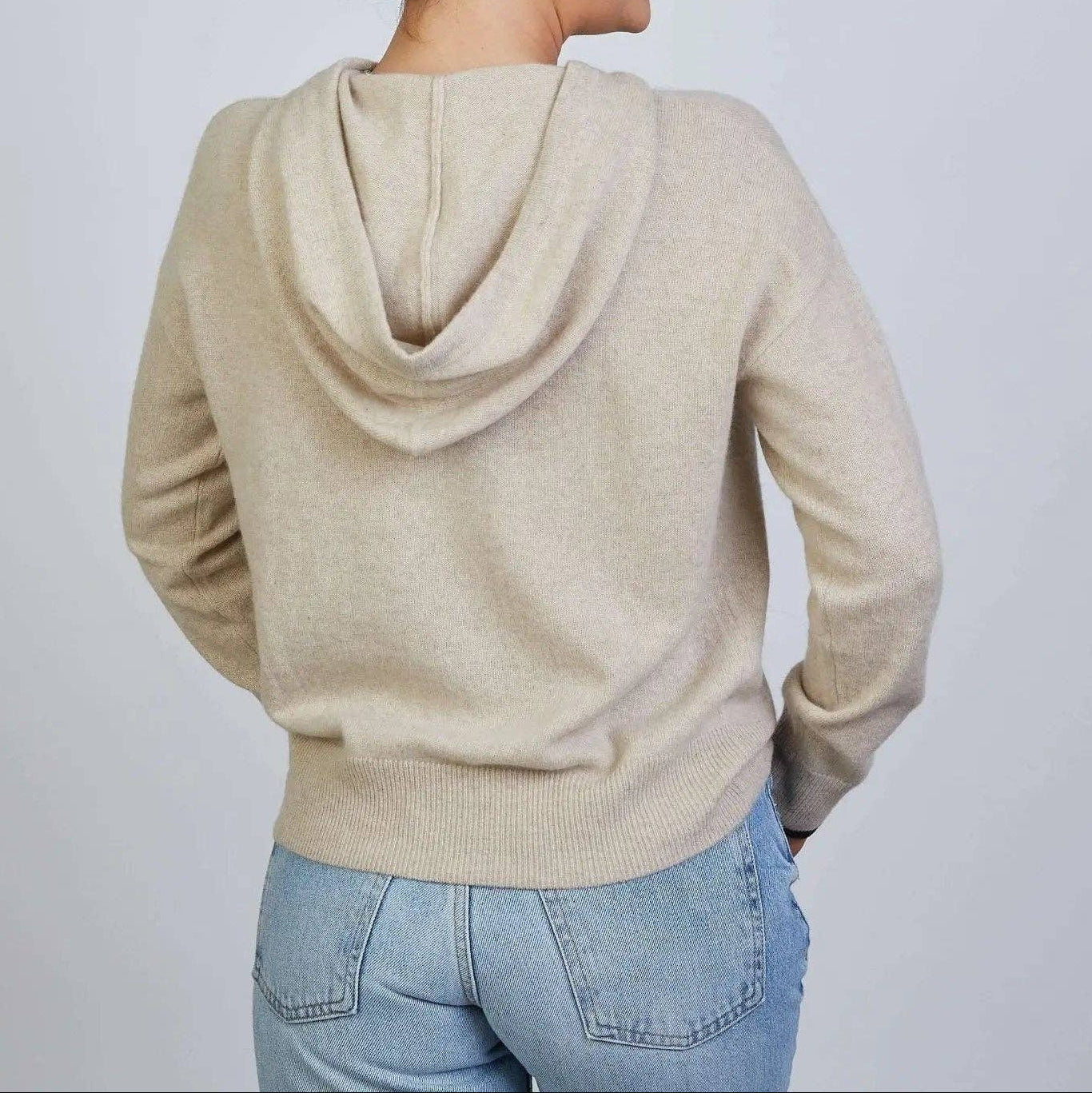 Woman wearing a beige hoodie and blue jeans against a plain background