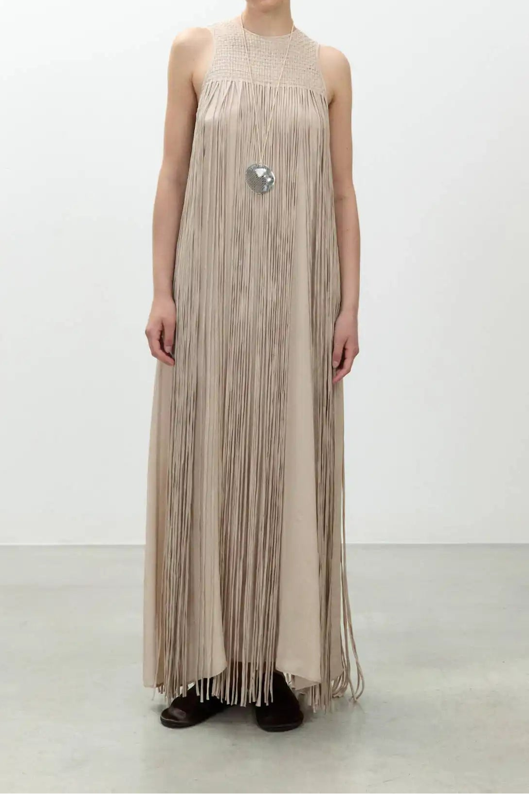 Woman wearing a long, pleated dress with a subtle pattern on a white background