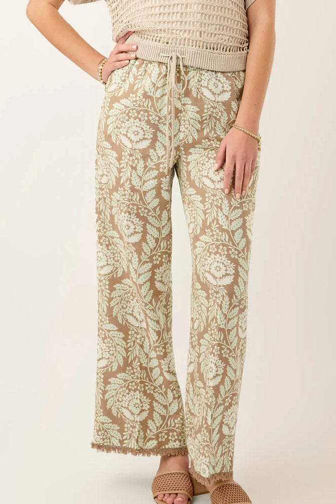 Woman wearing a beige crochet top and floral pants on a white background