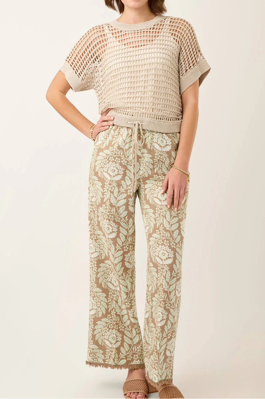 Woman wearing a beige crochet top and floral pants on a white background