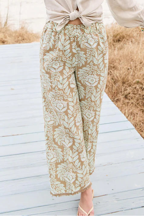 Woman in a beige shirt and patterned pants walking on a wooden boardwalk with grass and blue sky in the background