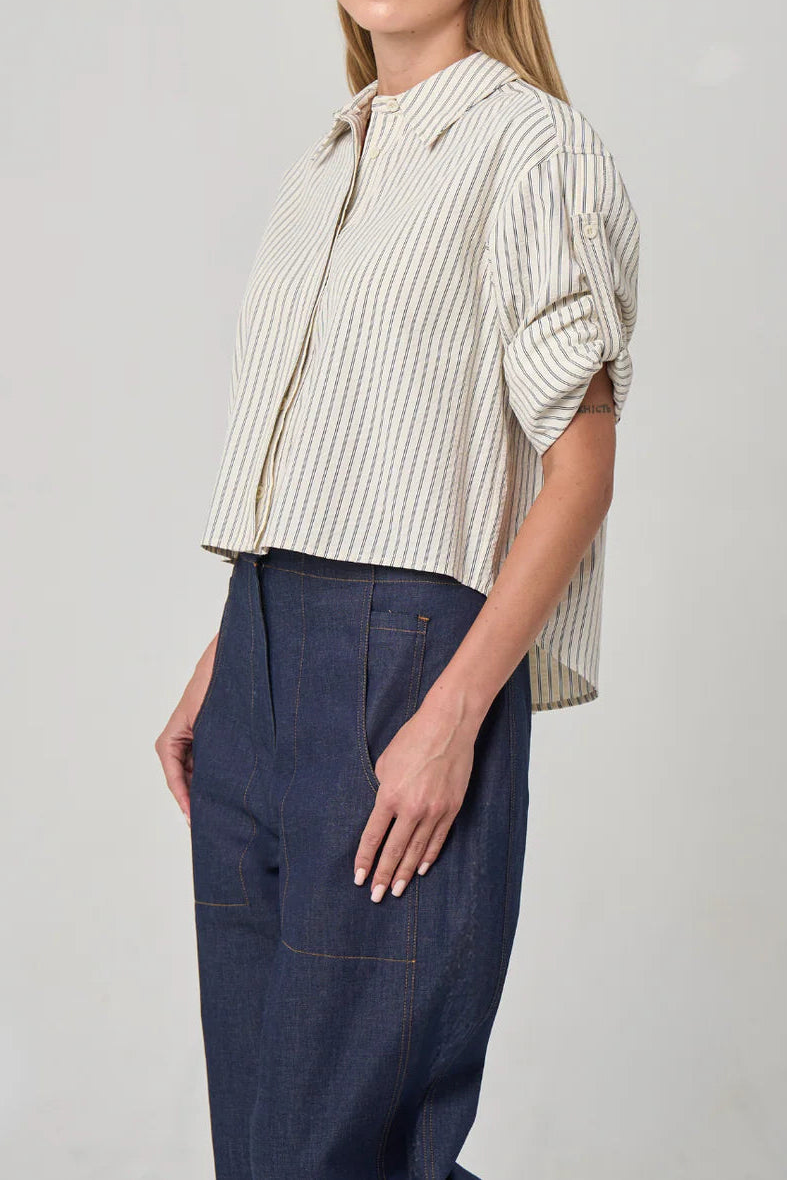 Woman wearing a striped shirt and dark pants against a plain background