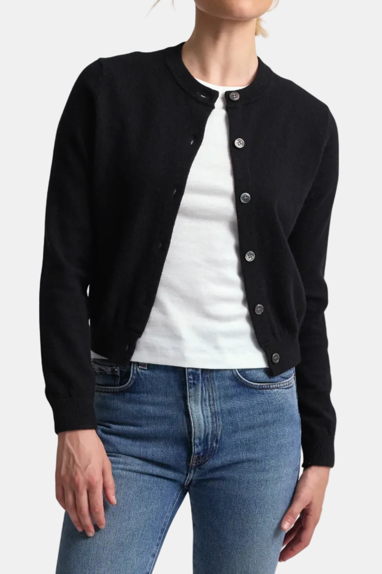 Person wearing a black cardigan over a white shirt and blue jeans on a white background