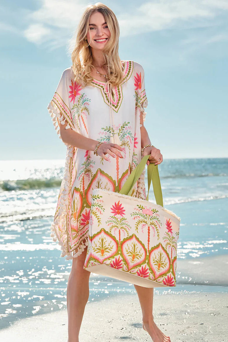 Woman in a colorful dress holding a matching tote bag on a beach.