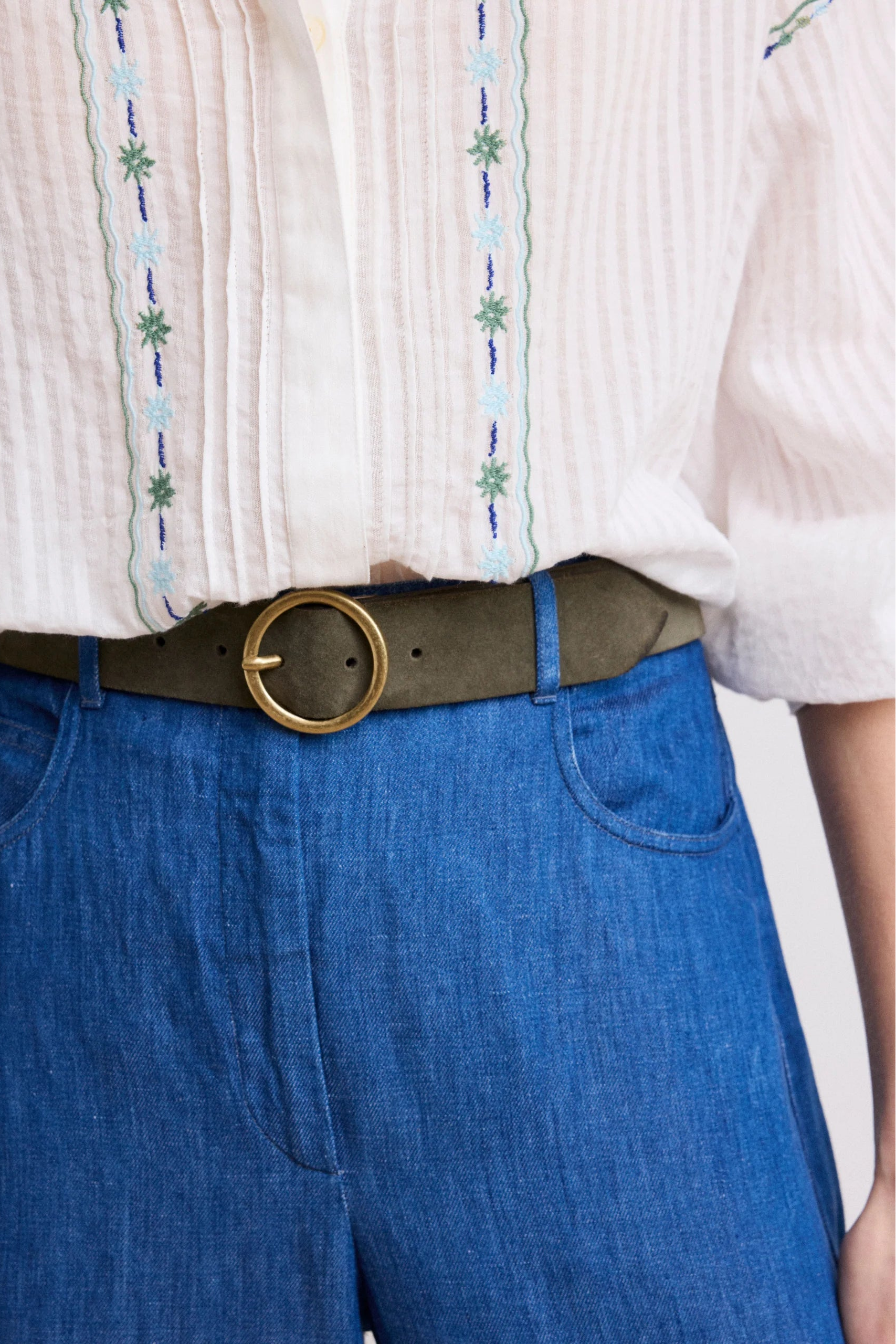 Person wearing a white shirt with embroidery and blue pants, focusing on the waist area.