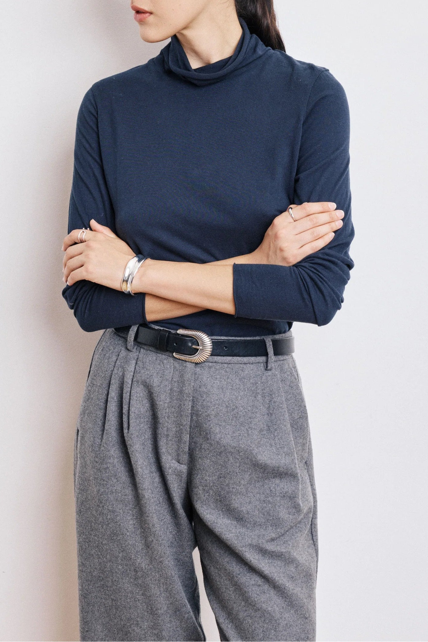 Woman wearing a navy turtleneck sweater and gray pants against a light background