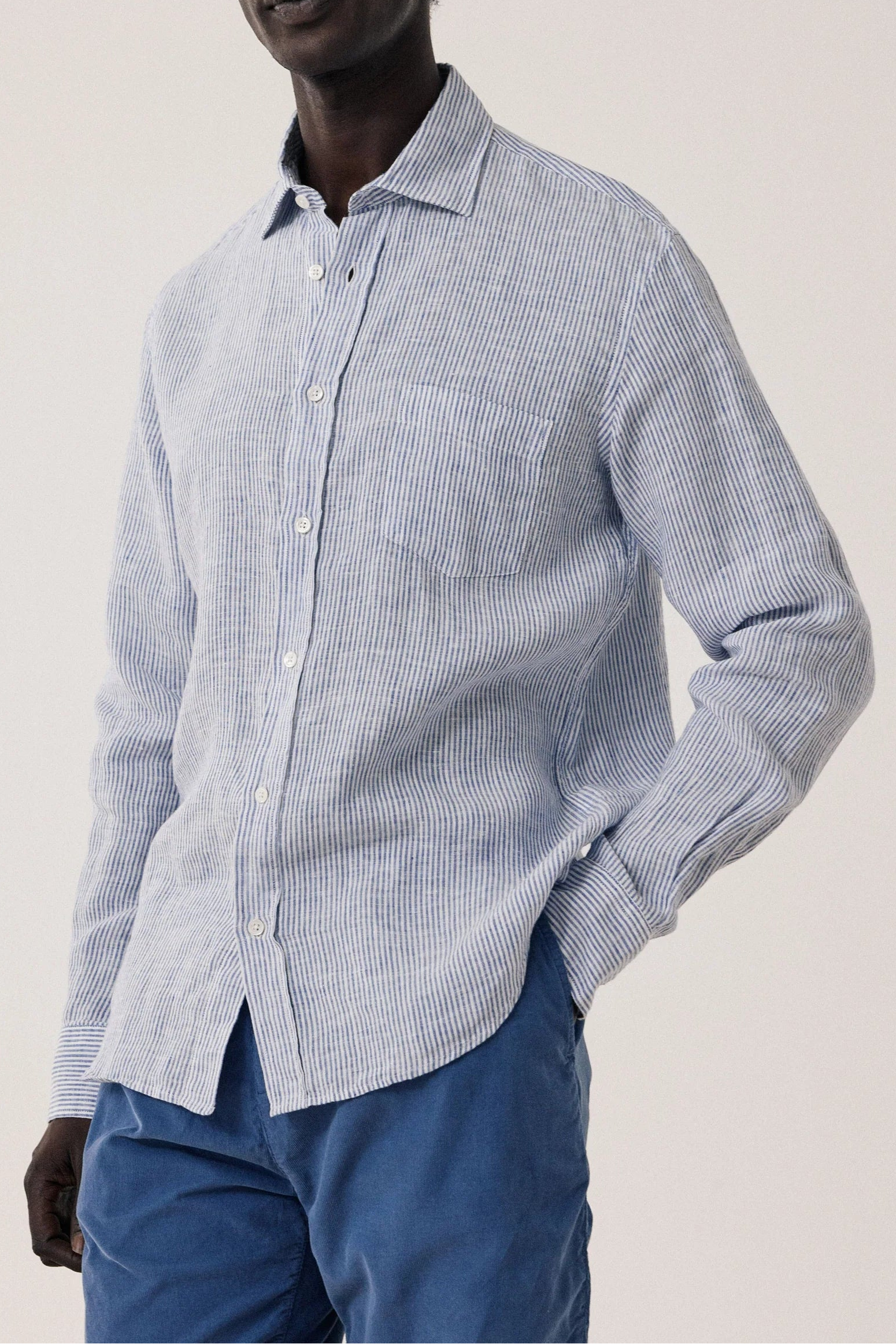 Man wearing a light blue checkered shirt and blue pants against a plain background