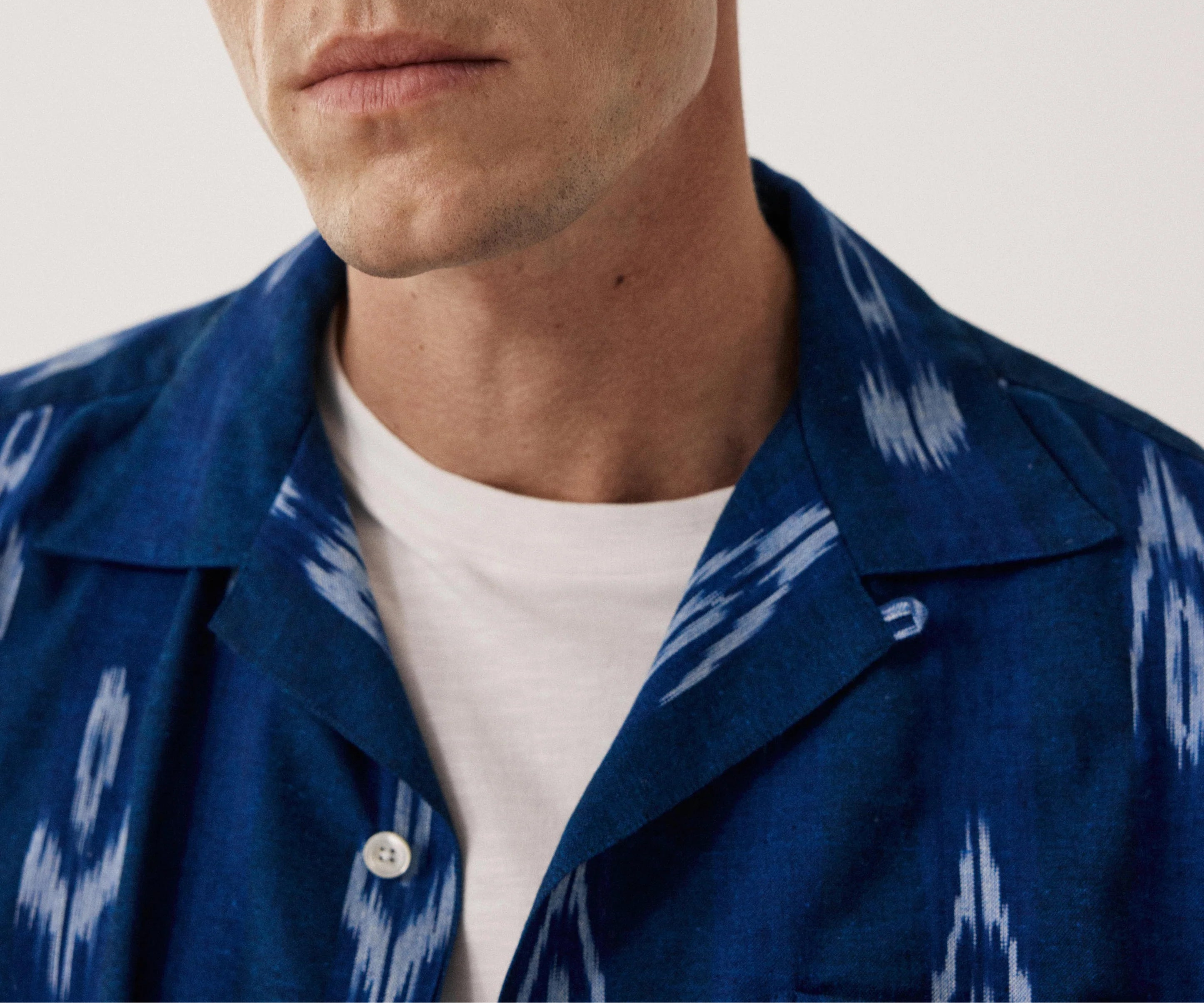 Man wearing a blue patterned shirt over a white shirt against a plain background