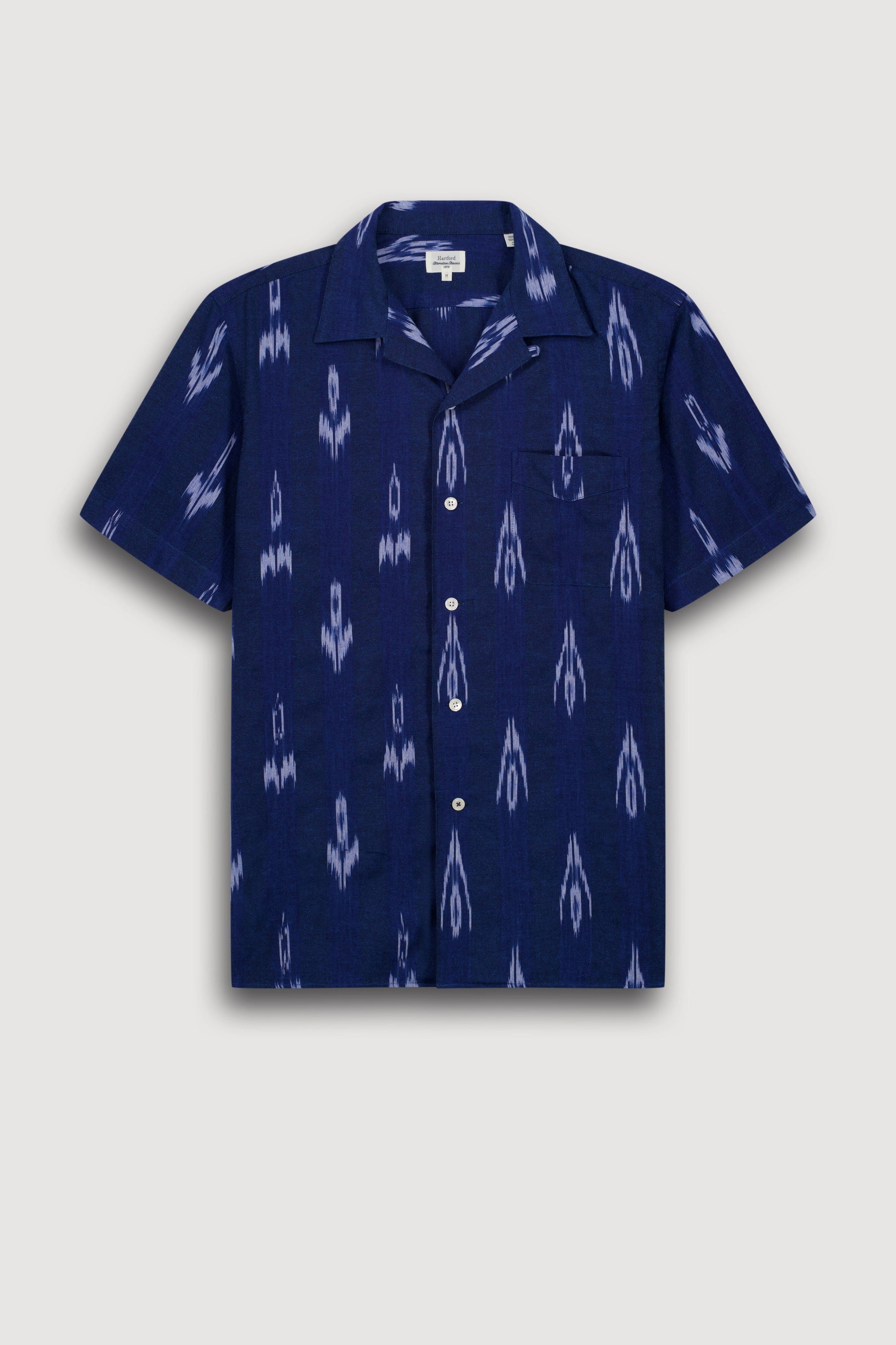 A short-sleeve button-up camp shirt in navy blue with a white ikat-style pattern, displayed flat against a light gray background.