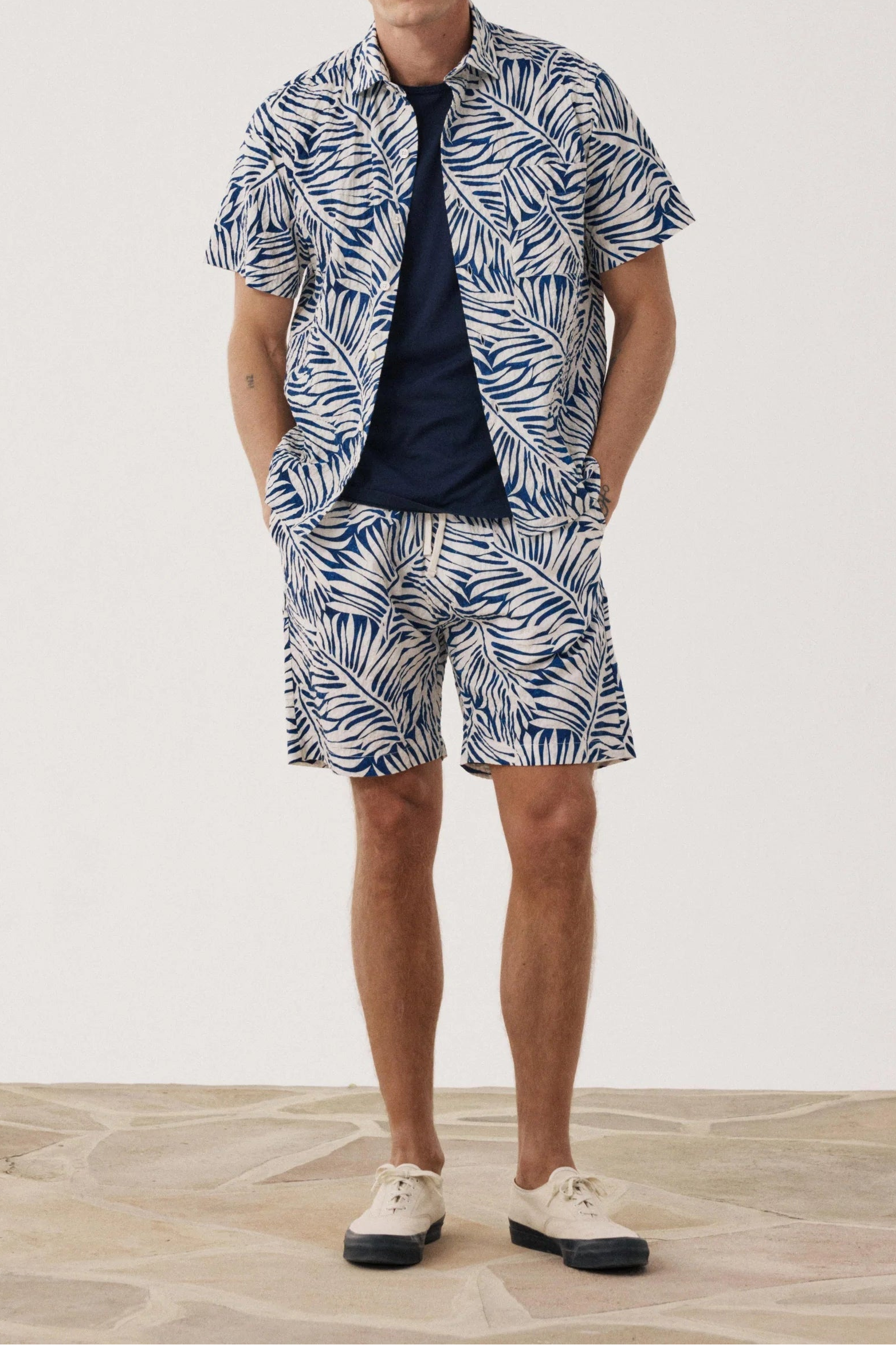 Man wearing a blue and white patterned shirt and shorts on a light background