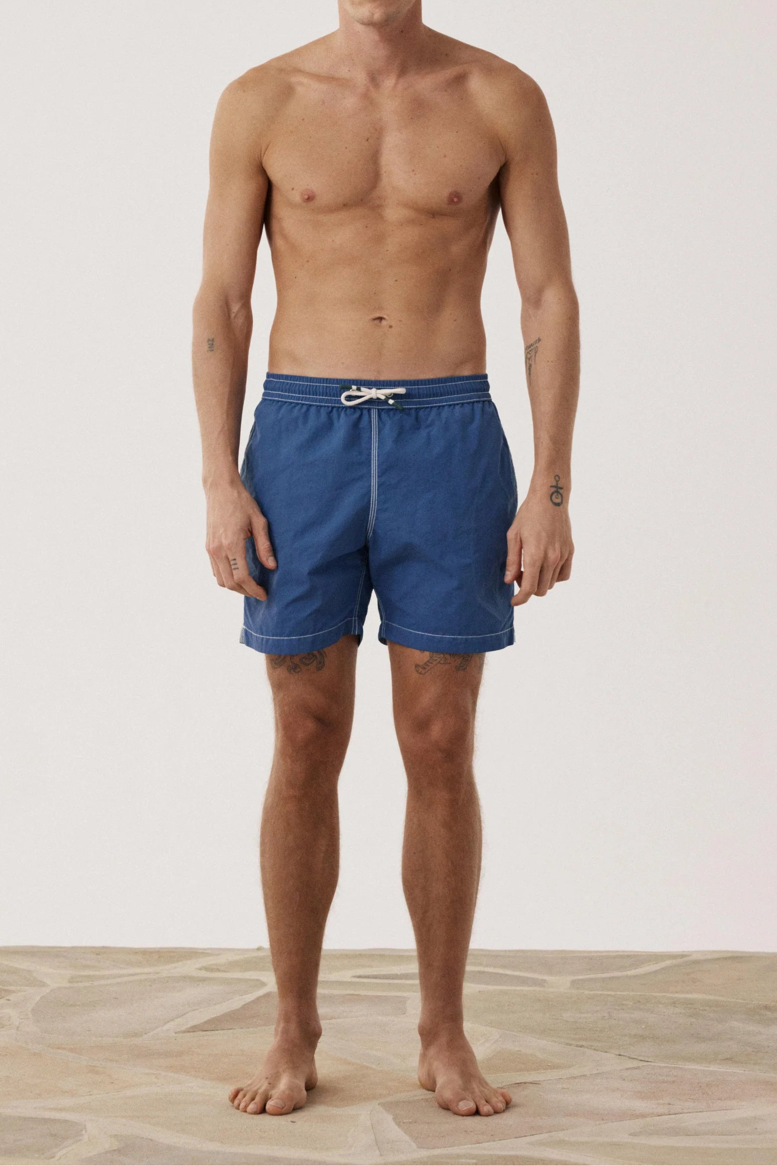 Man wearing blue swim shorts on a neutral background