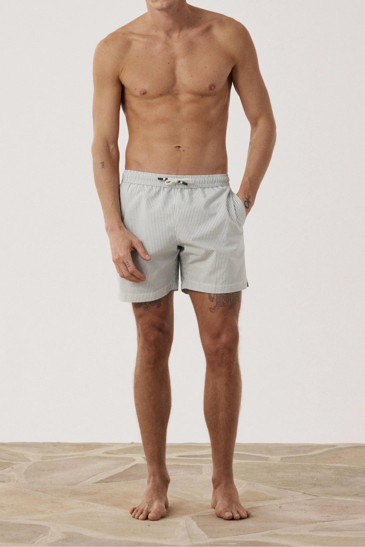 Man wearing light gray swim shorts standing against a plain background