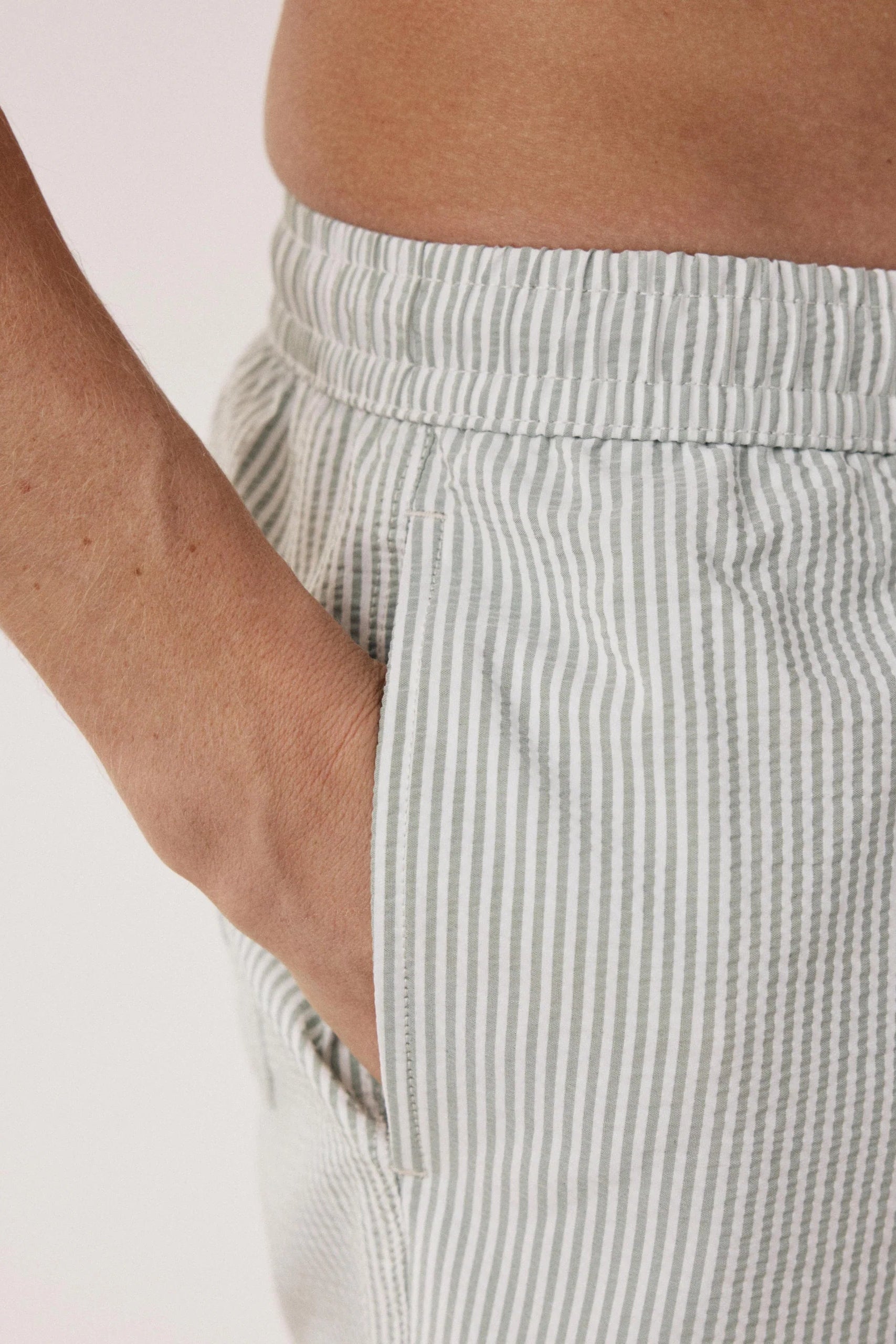 Close-up of a person wearing light gray and white vertically striped lounge shorts, with one hand in the side pocket and the waistband visible.