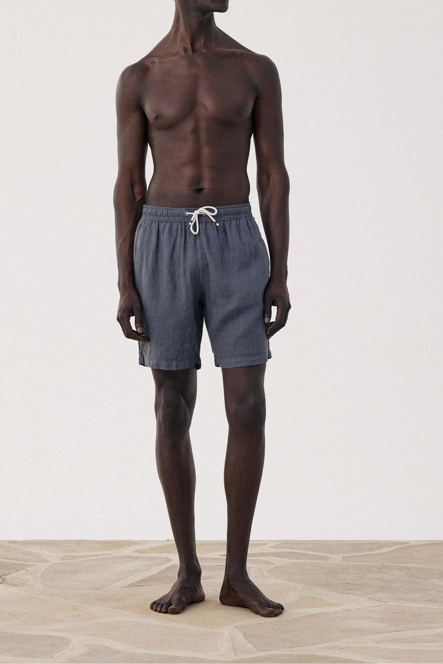 Man wearing gray shorts standing on a light wooden floor with a white background