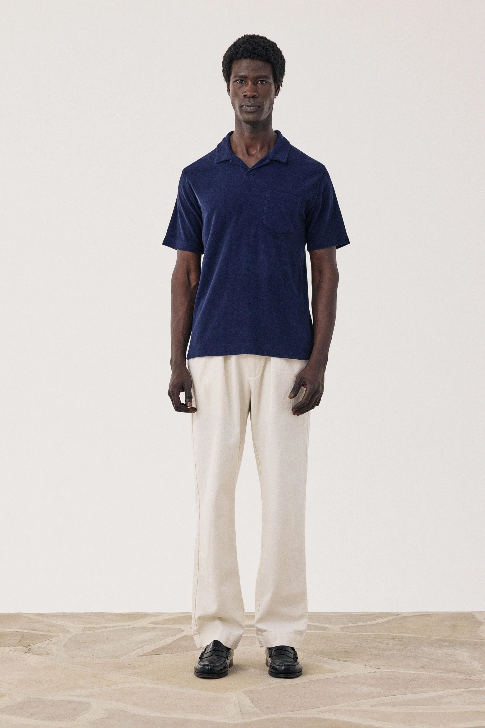 Man wearing a navy polo shirt and beige pants standing against a white background