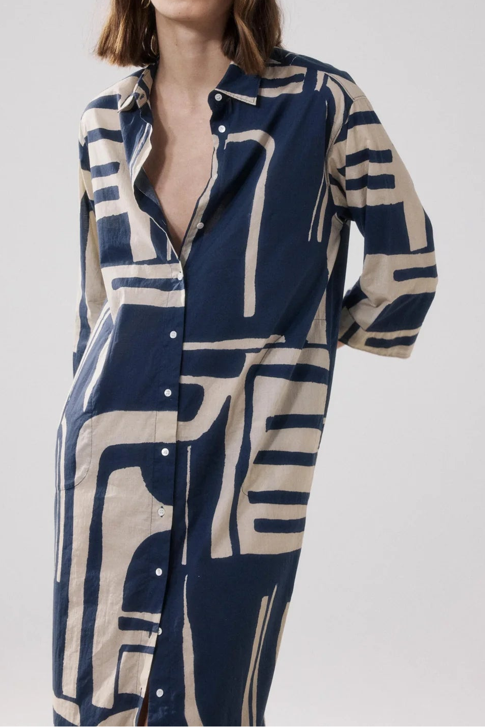Woman wearing a long, patterned shirt dress with abstract design on a plain background