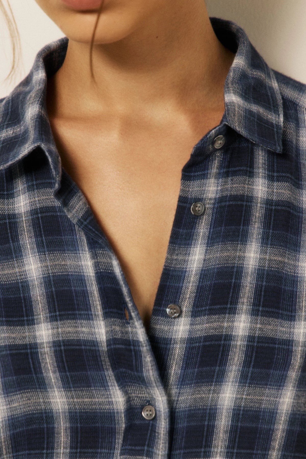 Close-up of a person wearing a navy and white plaid button-up shirt, showing the collar, chest area, and fabric texture.