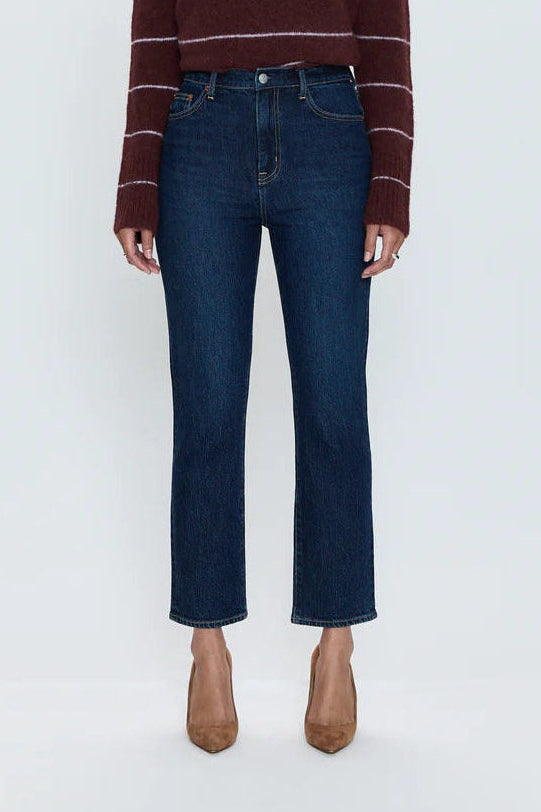 A model stands against a light gray studio background wearing a burgundy and white striped knit sweater, dark blue straight-leg jeans, and tan pointed-toe heels.