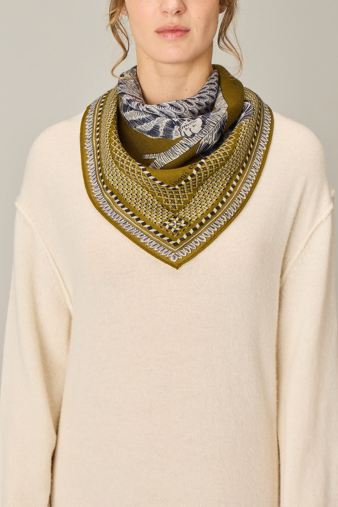 Woman wearing a cream sweater and patterned scarf against a plain background