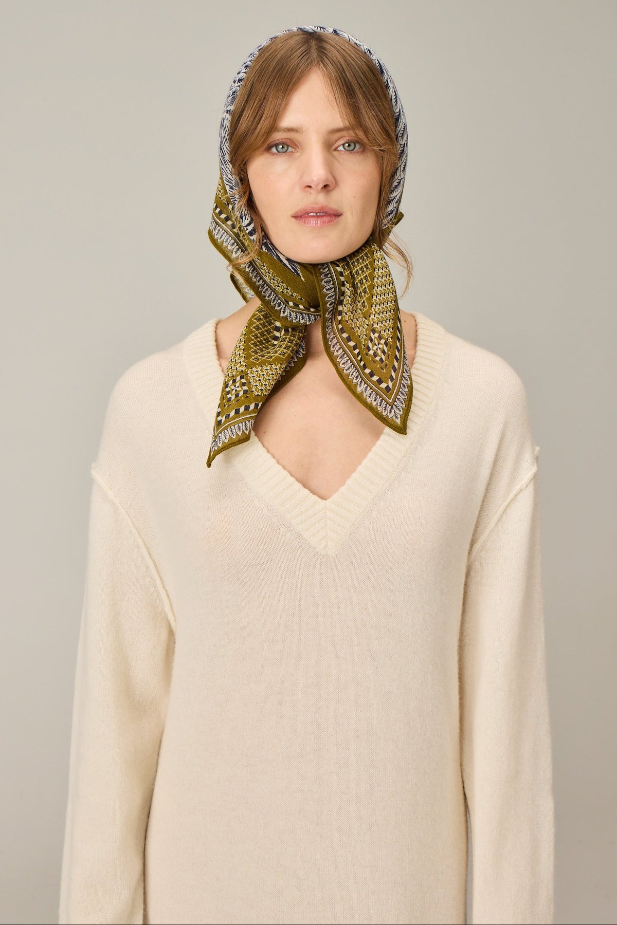 Woman wearing a green patterned headscarf on a plain background