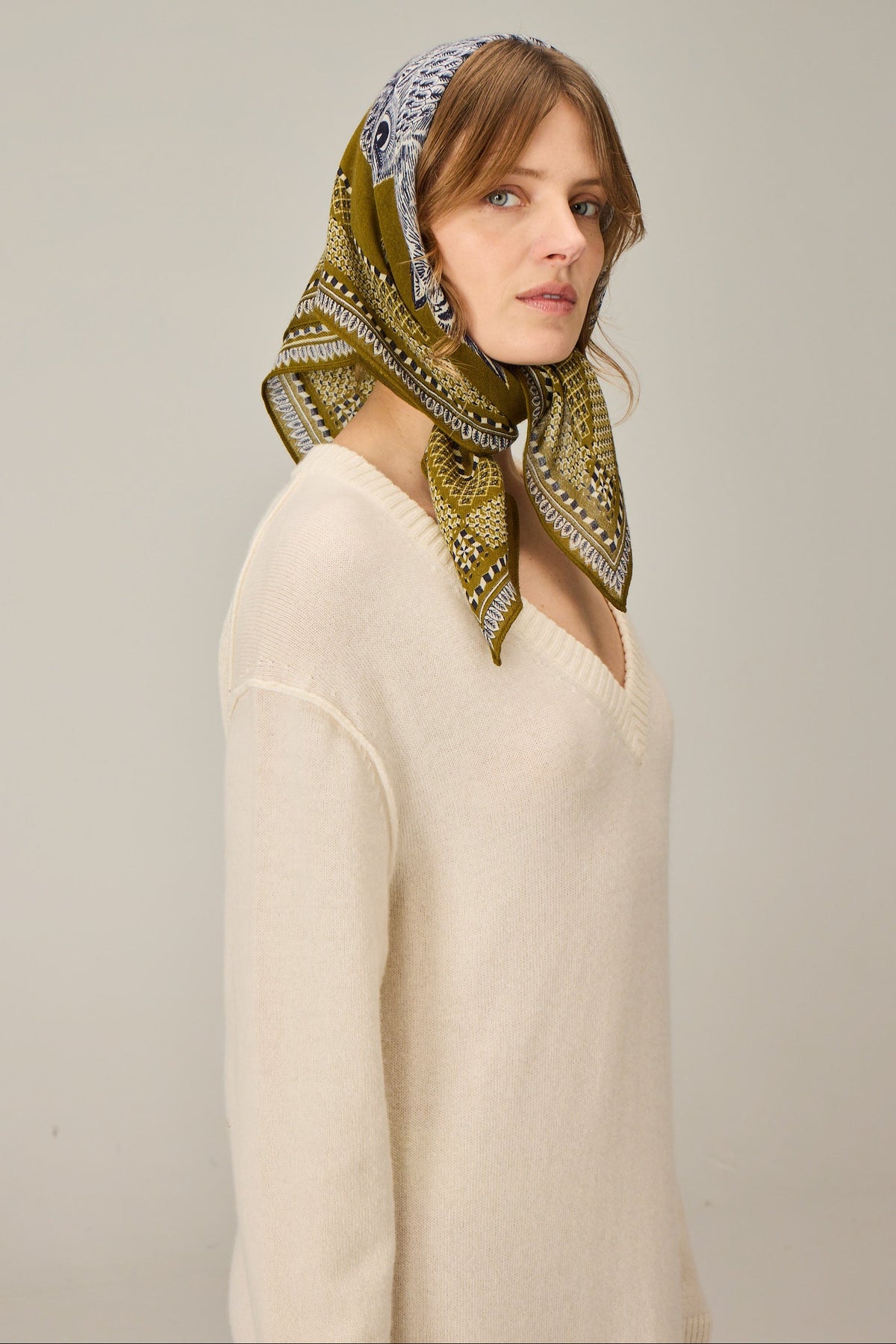 Woman wearing a patterned green scarf on a plain background