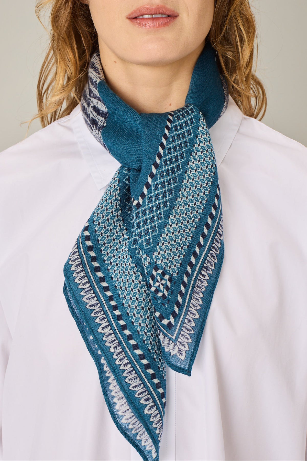 A close-up of a woman wearing a white shirt and a teal blue patterned scarf tied around her neck.