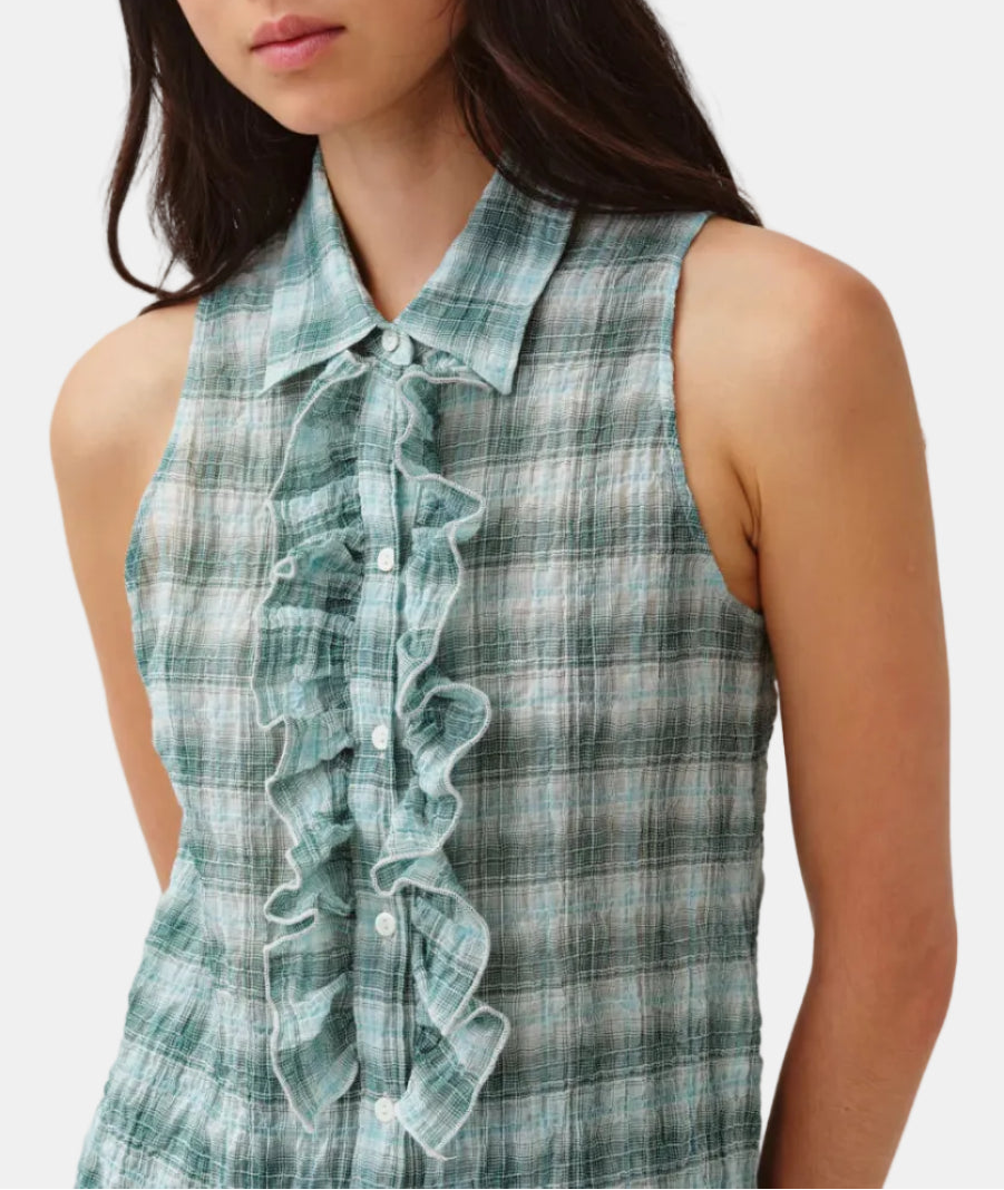 Woman wearing a green plaid blouse with ruffled details on a white background