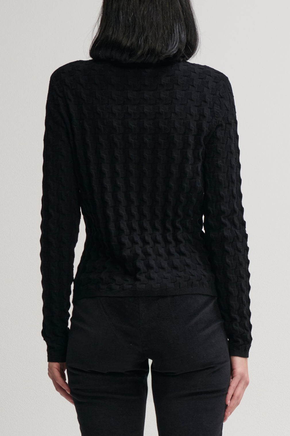 Person wearing a black textured sweater against a plain background
