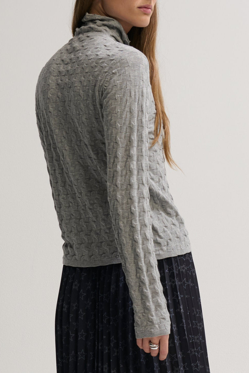 Woman wearing a gray cable knit sweater against a plain background
