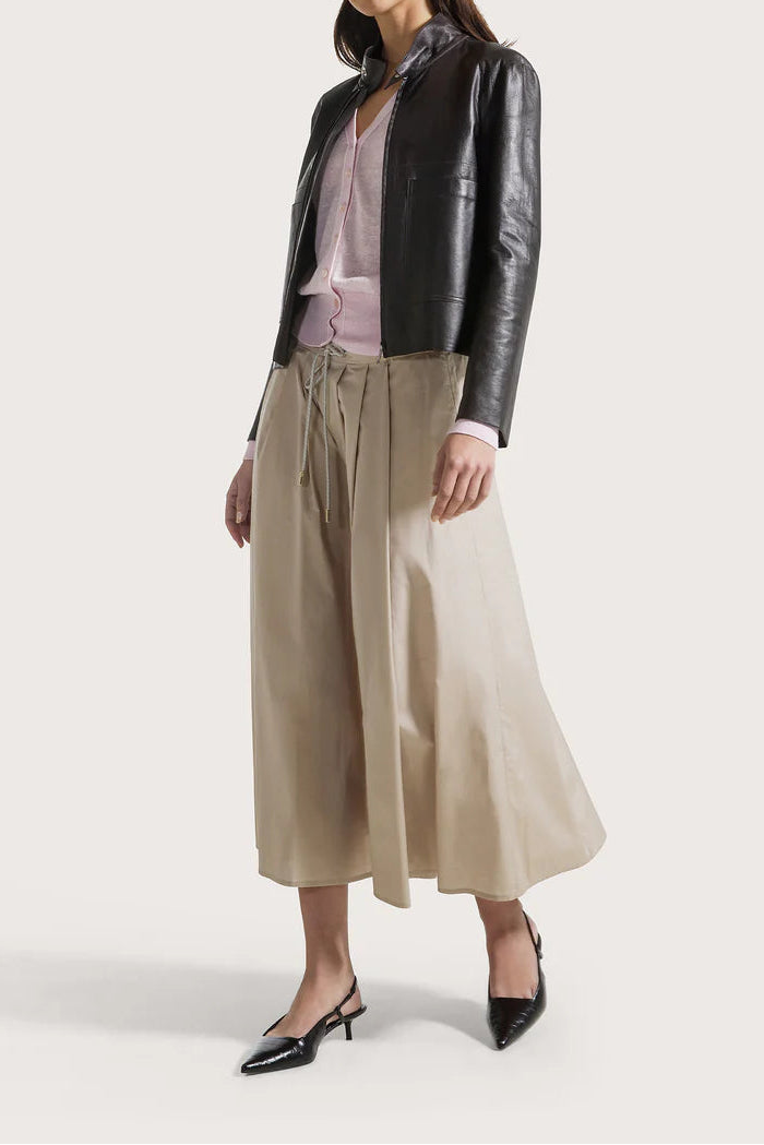 Woman wearing a black leather jacket, light pink top, beige wide-leg pants, and black shoes on a white background