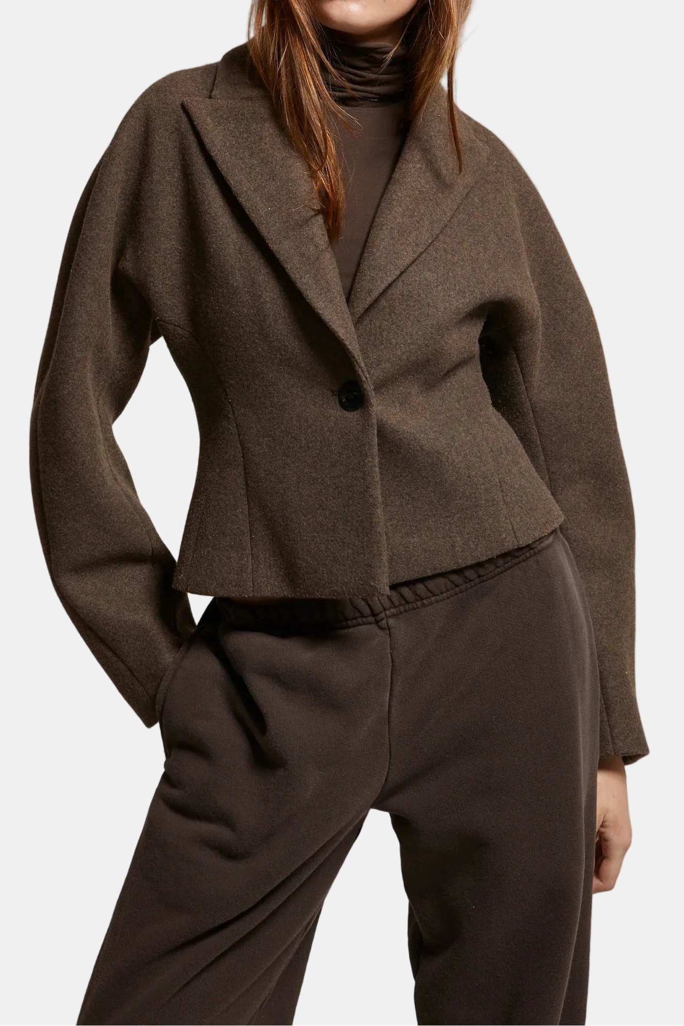 Woman wearing a brown coat and sunglasses against a plain background