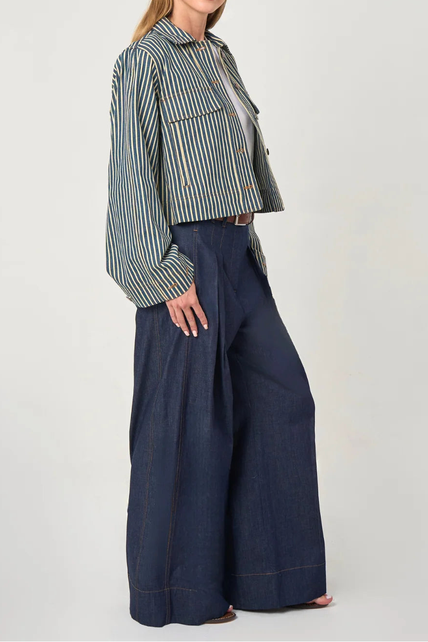 A woman modeling a cropped, long-sleeve striped button-up shirt in green and white, paired with dark wide-leg denim pants, against a plain light gray studio background.